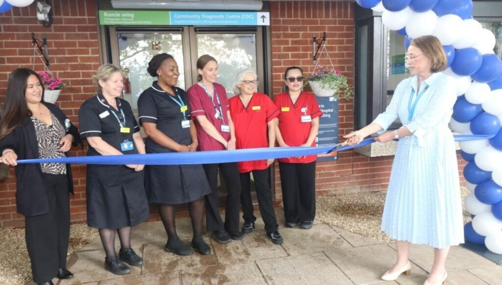 6 people stood in front of St Albans Hospital with a ribbon in front of them being cut.