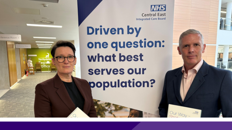 Jan Thomas and Robin Porter standing in front of a pull up banner saying "one question: what best serves our population?"