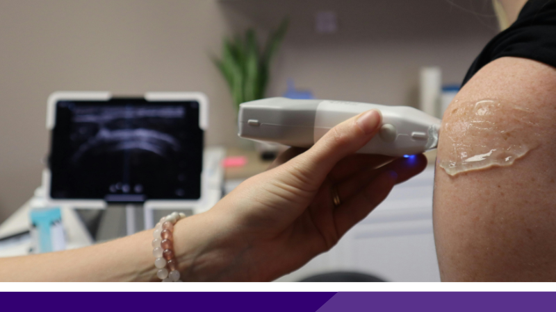 Close up of an individual's partially exposed left shoulder with gel on it while a hand holding an ultrasound device rubs over it.