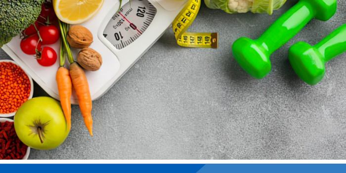 Fruit and dumbbells on weighing scales and tape measure to show healthy weight.