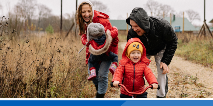 A family of 4 laughing together outdoors in the rain whilst out for a walk and bike ride