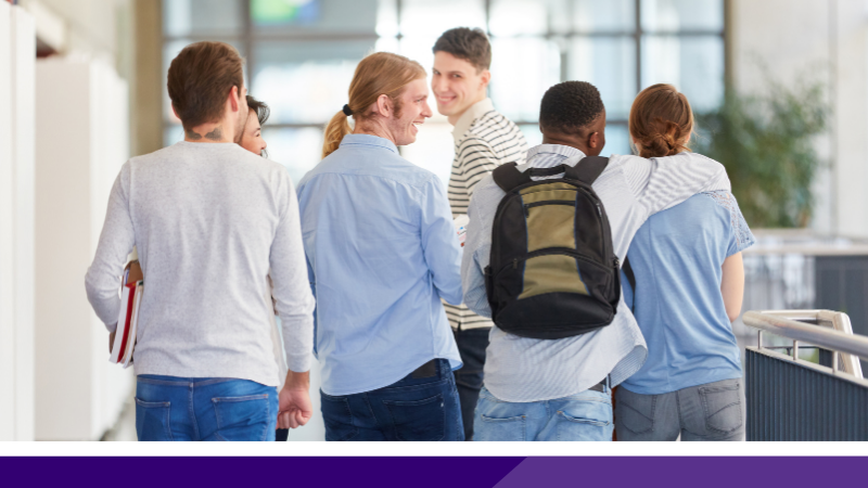 Six students walking together with their backs to the camera. Two are looking back smiling and two have their arms around each other in a friendly way.